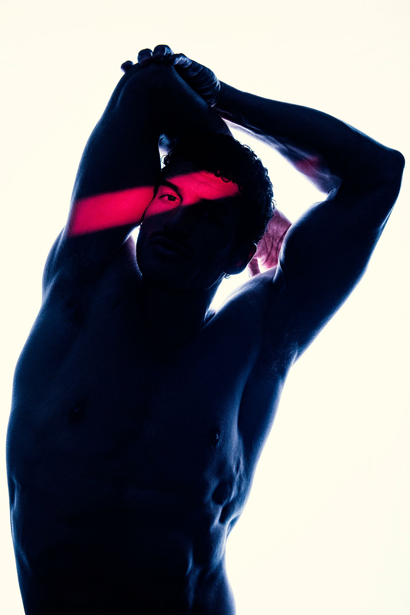 Muscular shirtless man posing with arms raised, dramatic blue lighting with red stripe across face.