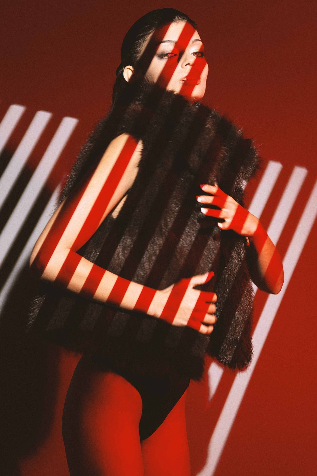 Woman in fur vest with bold stripe light pattern on red background.