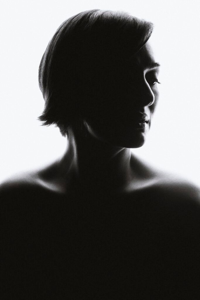 Dramatic black and white silhouette portrait of a woman with short hair against bright white background.