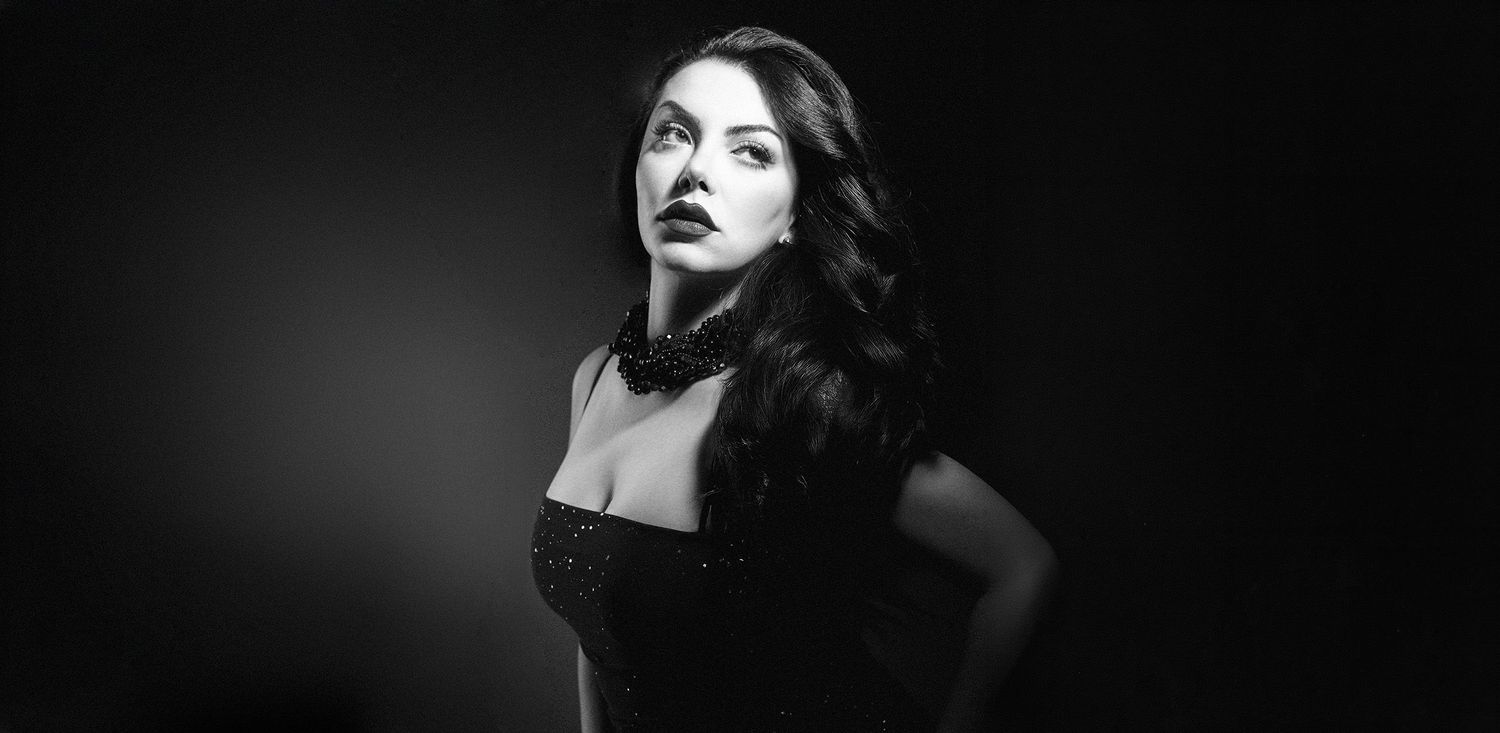 Black and white portrait of glamorous woman in black dress with bold makeup.