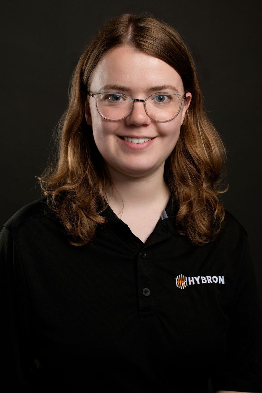 Young woman in black Hybron polo shirt wearing glasses, corporate headshot portrait.