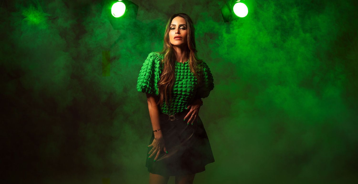 Woman in green houndstooth puff-sleeve top and black skirt posing under green stage lights with smoke.