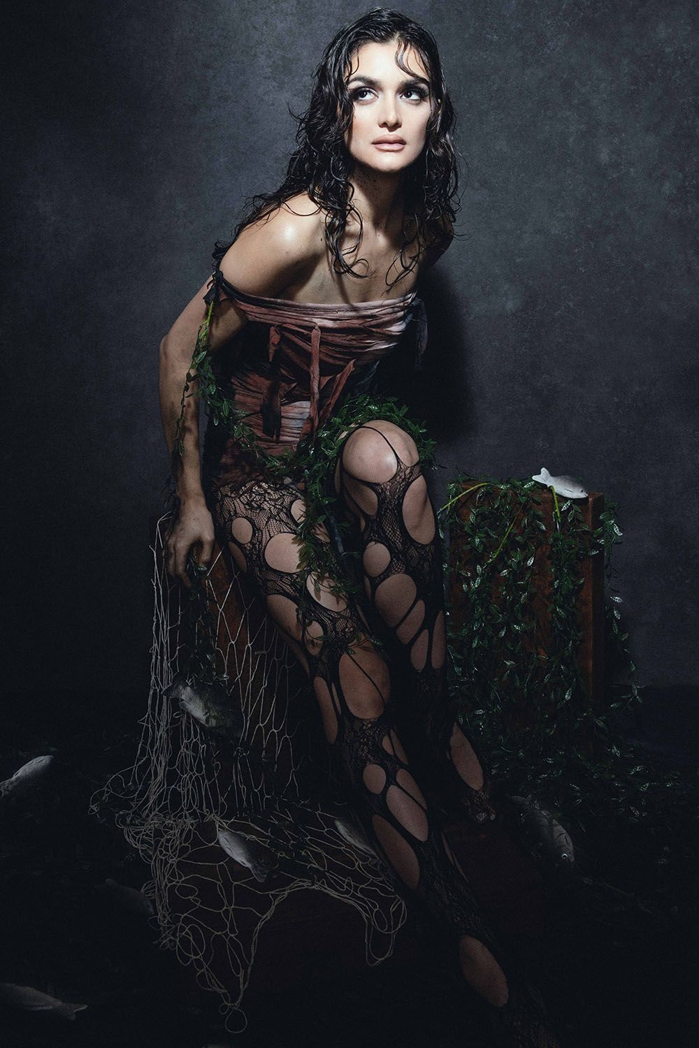 Dark artistic portrait of woman in corset and fishnet bodysuit with ivy and fishing net props.