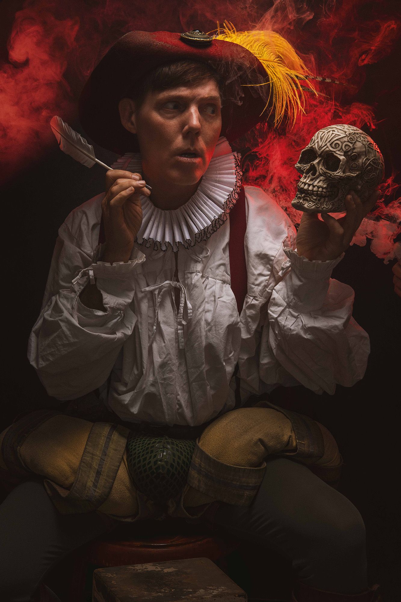 Renaissance man in period costume holds skull and quill pen, surrounded by dramatic red smoke on dark background.