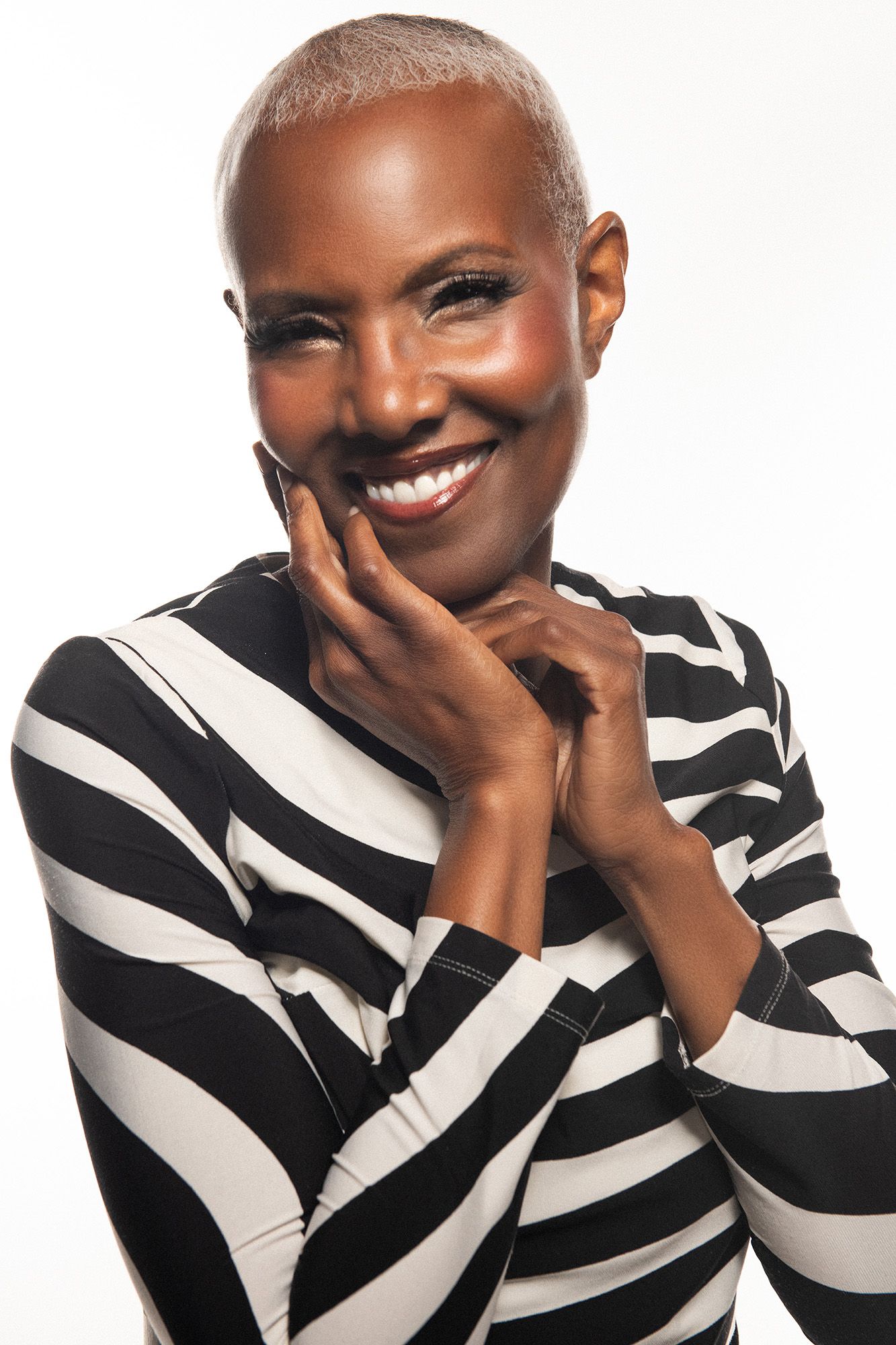 Smiling Black woman with short hair wearing a black and white striped top, posing with hand on chin against white background.