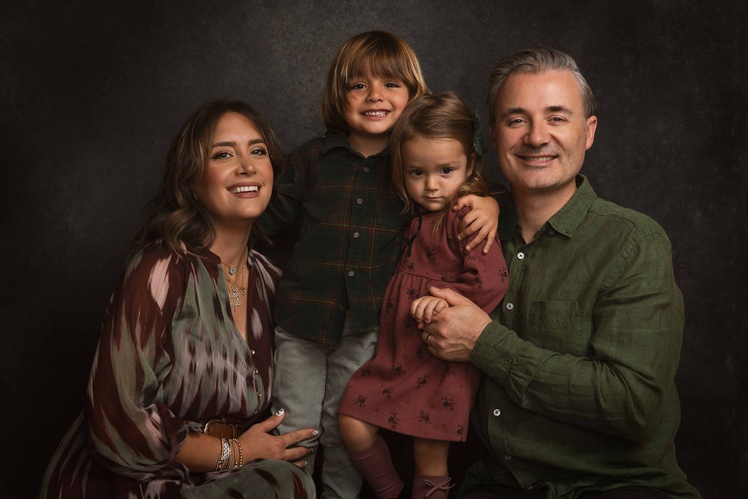 Smiling family of four posing for a professional studio portrait on a dark background.