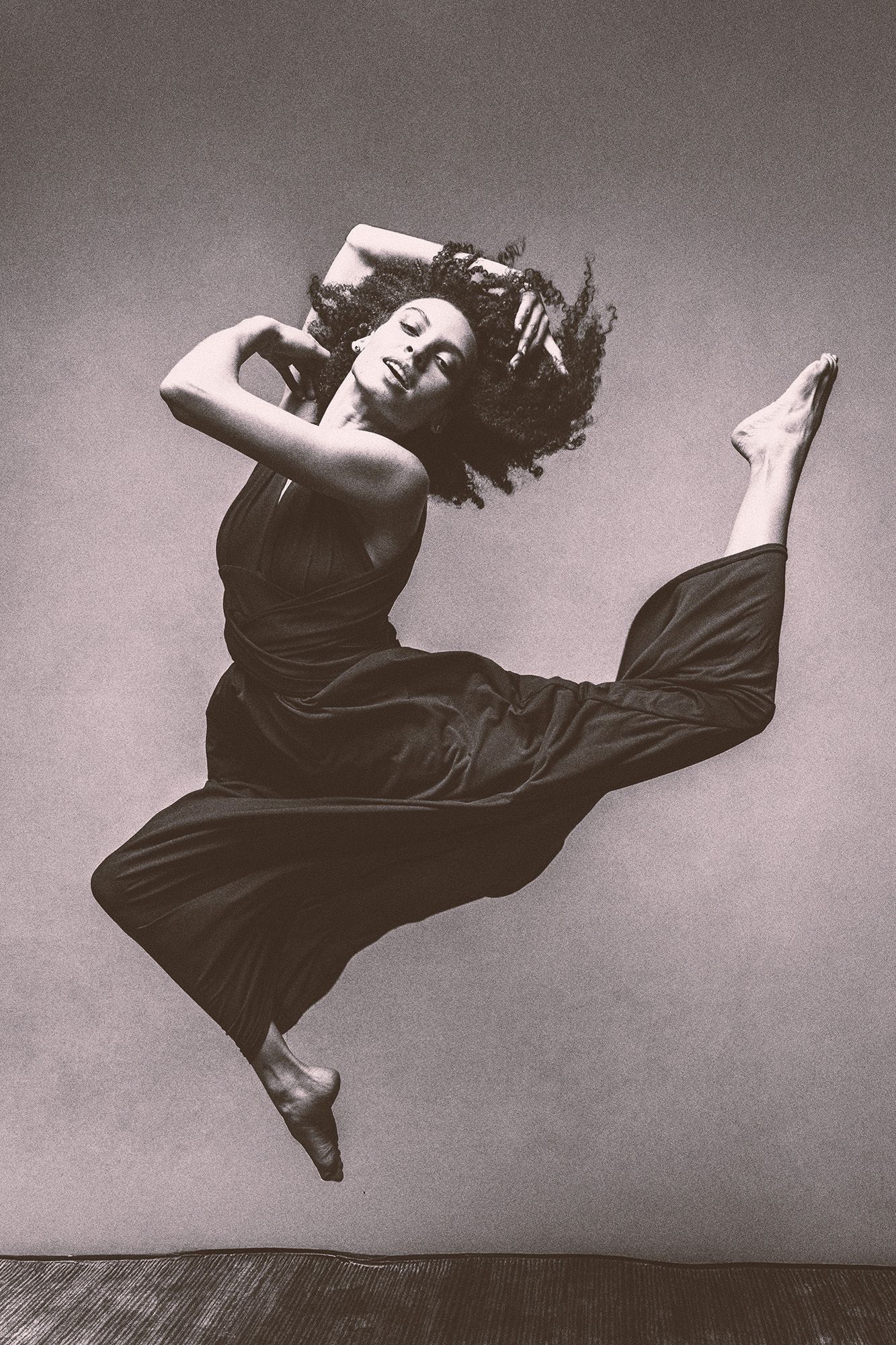Black and white photo of dancer leaping gracefully in black outfit.
