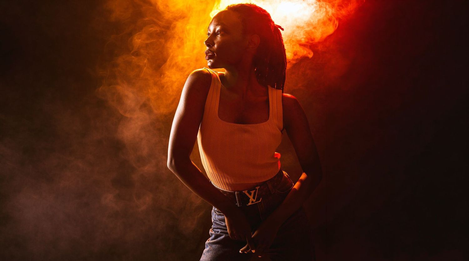 Woman in white tank top dances in dramatic orange smoky stage lighting atmosphere.