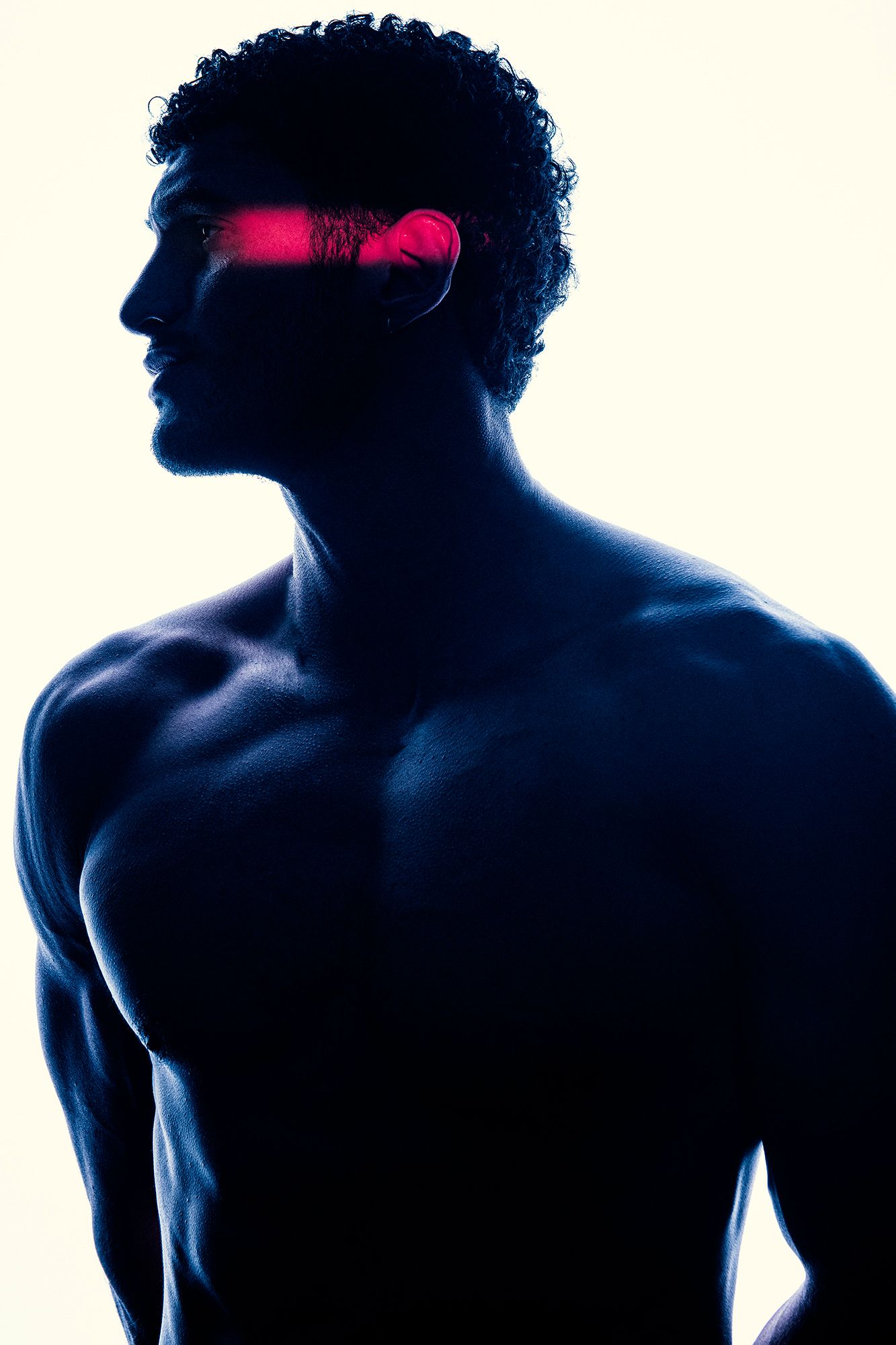 Muscular man silhouetted in blue light with glowing red visor effect across eyes against white background.
