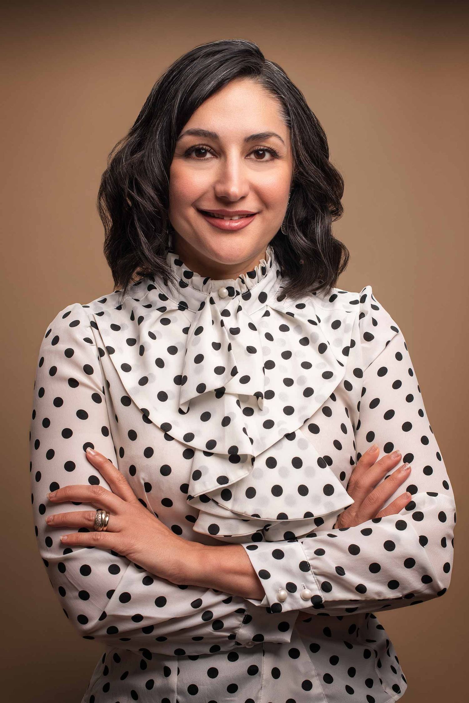 Professional woman in a polka dot blouse with arms crossed smiling against a beige background.