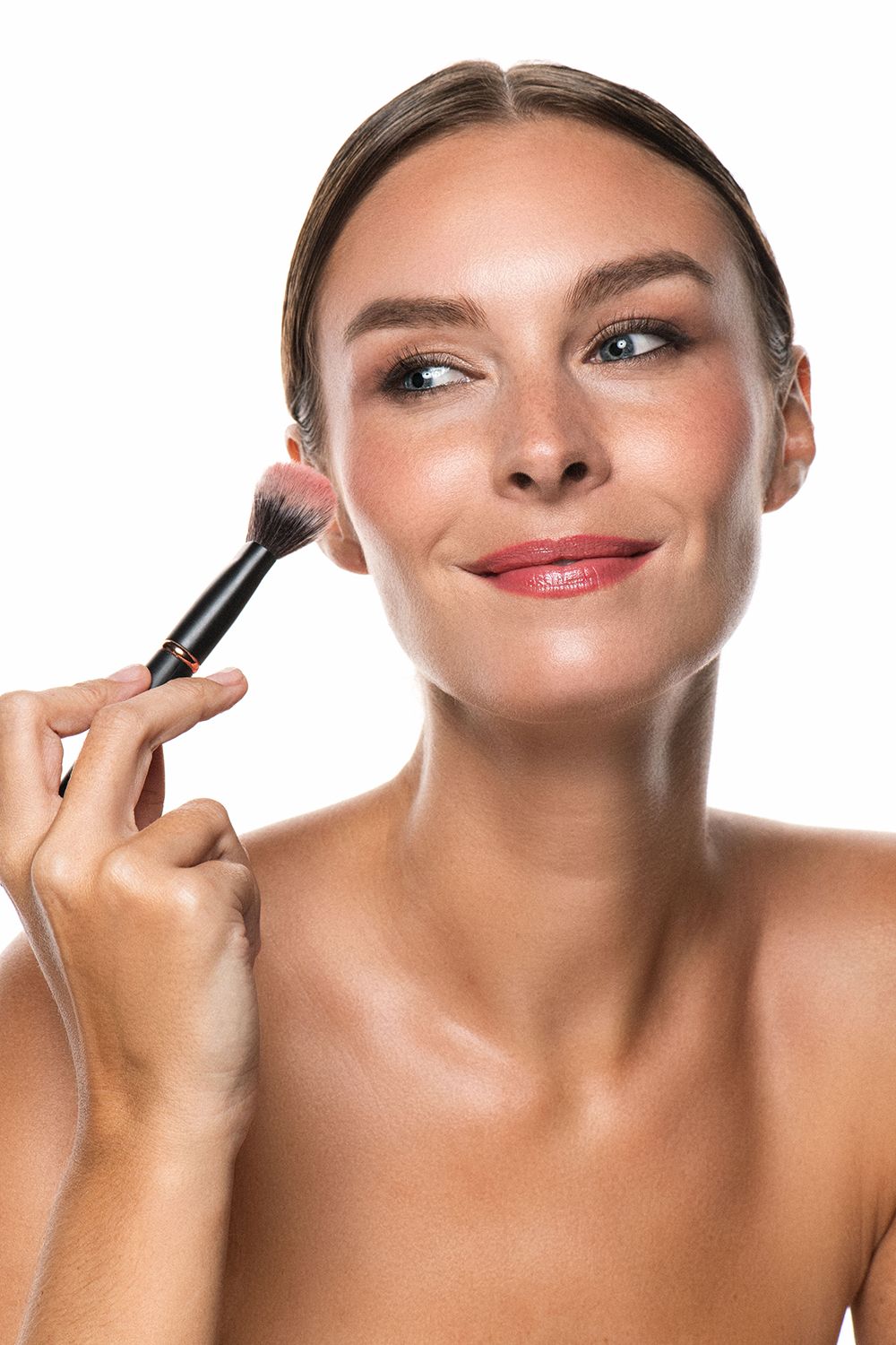 Smiling woman applying blush with a makeup brush on a white background.