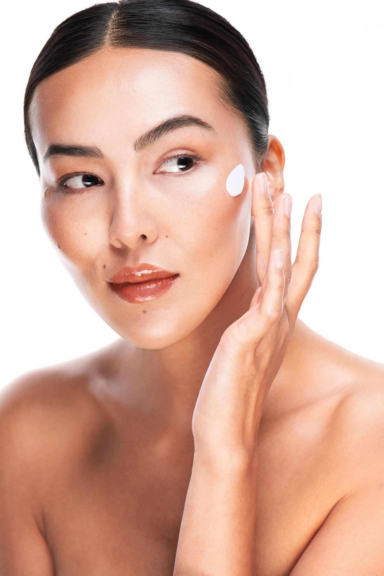 Young Asian woman applying white face cream to cheek, beauty skincare routine on white background.