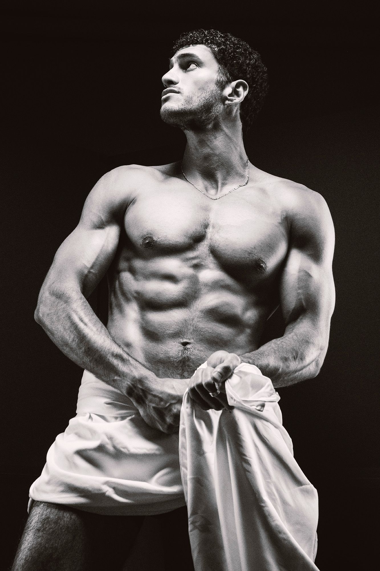 Black and white photo of muscular shirtless man holding white fabric.