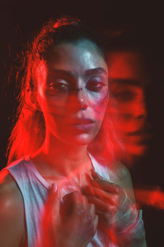Artistic double exposure portrait of a woman illuminated by red light in a dark studio setting.