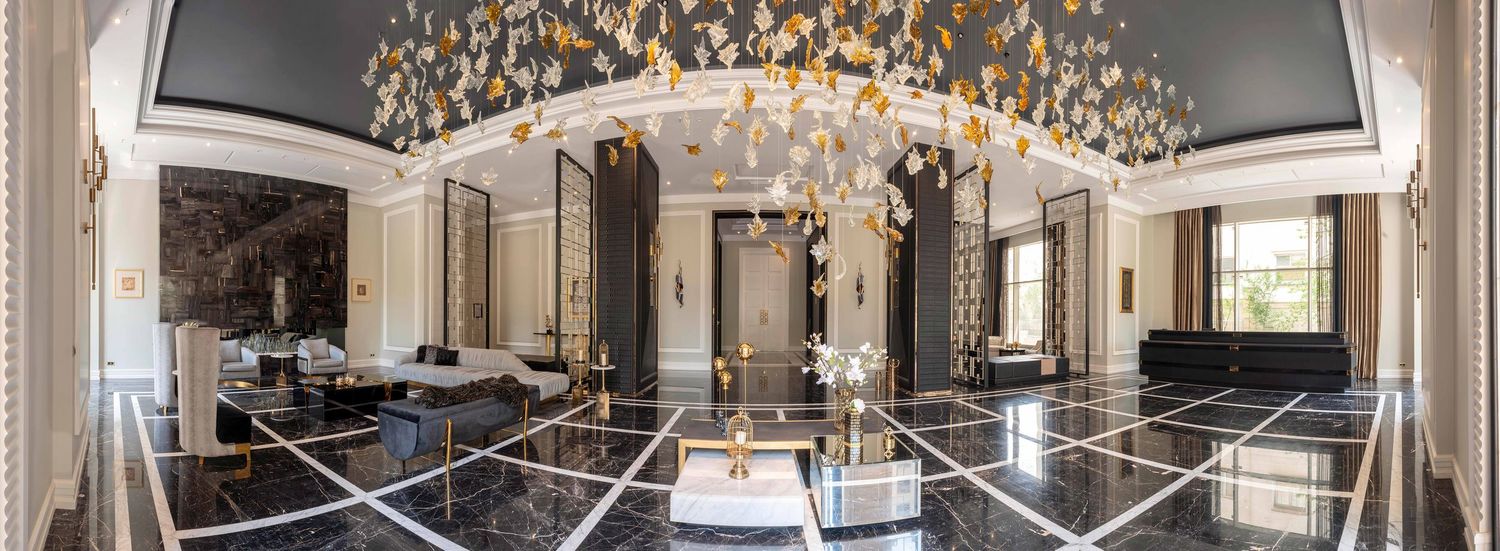 Luxurious hotel lobby with marble floors, ornate gold chandelier, and elegant dark ceiling with floral motifs.