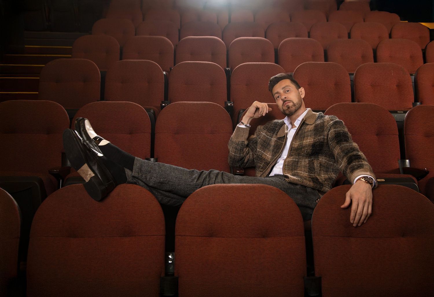 Relaxed man sitting in empty red theater seats with legs propped up.