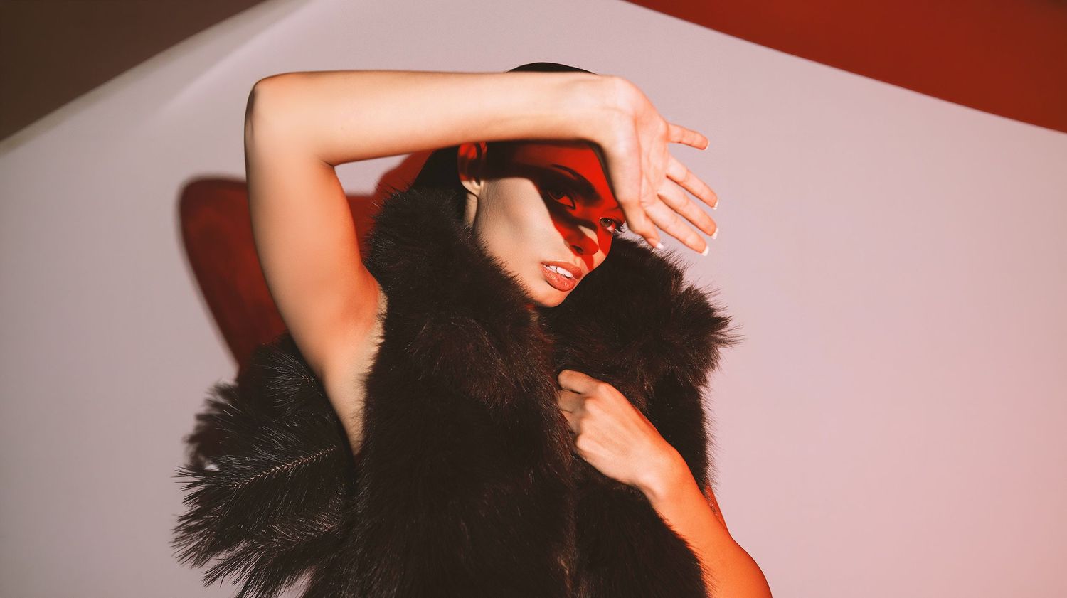 Fashion model in black fur vest wearing red sunglasses posing in a studio setting.