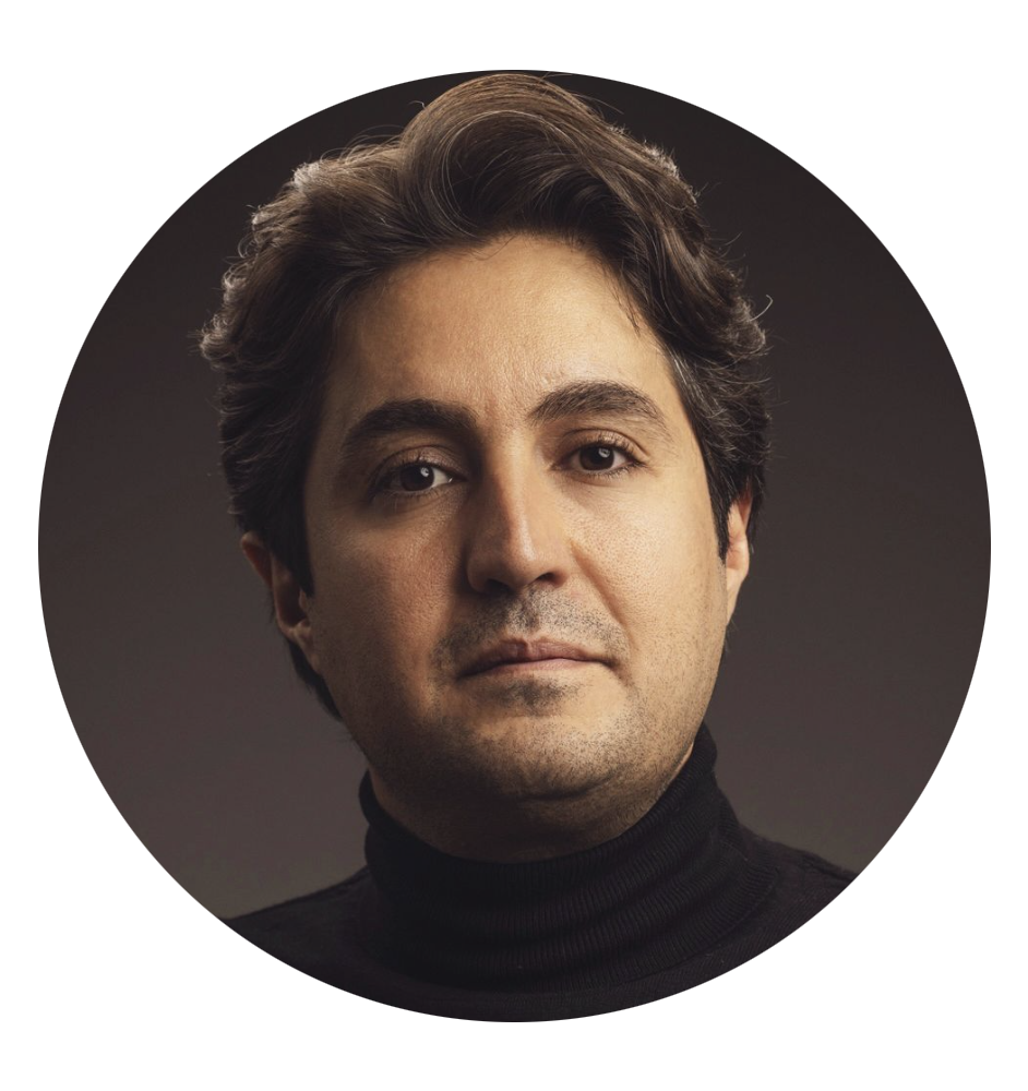 Professional headshot of a man with dark wavy hair wearing a black turtleneck against a dark background.