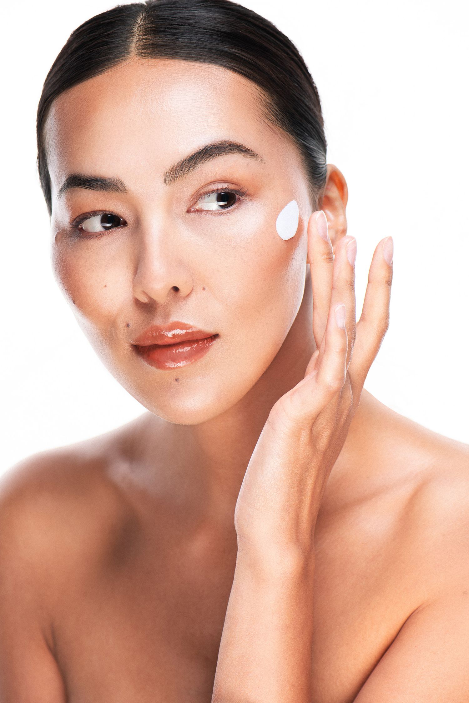 Woman applying white face cream to her cheek, showcasing a skincare beauty routine against a white background.