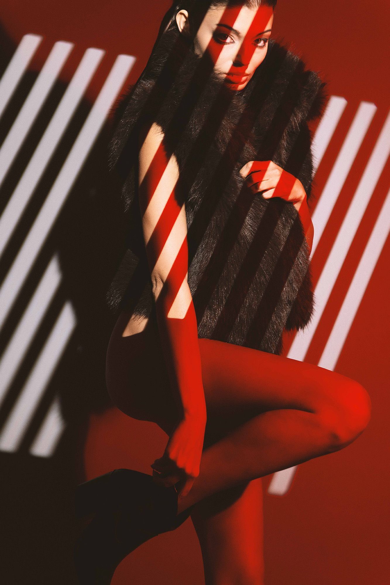 Woman in fur vest with dramatic stripe shadows on red background.
