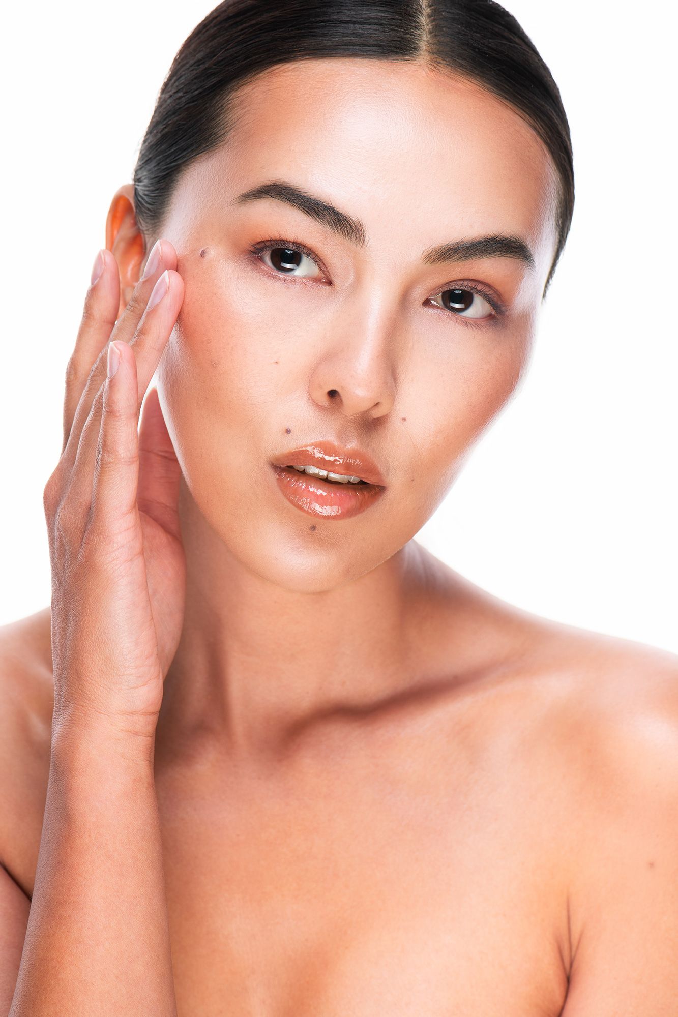 Young Asian woman with glowing skin touching her cheek, beauty and skincare concept on white background.