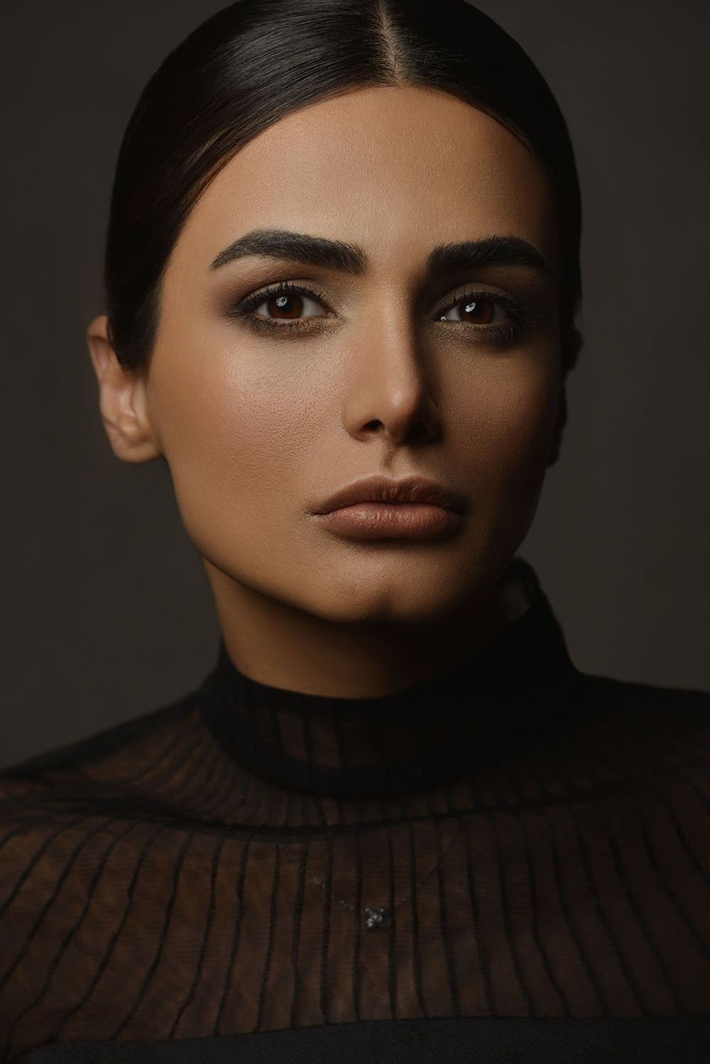 Close-up portrait of a woman with bold brows and bronze makeup wearing a black turtleneck top.