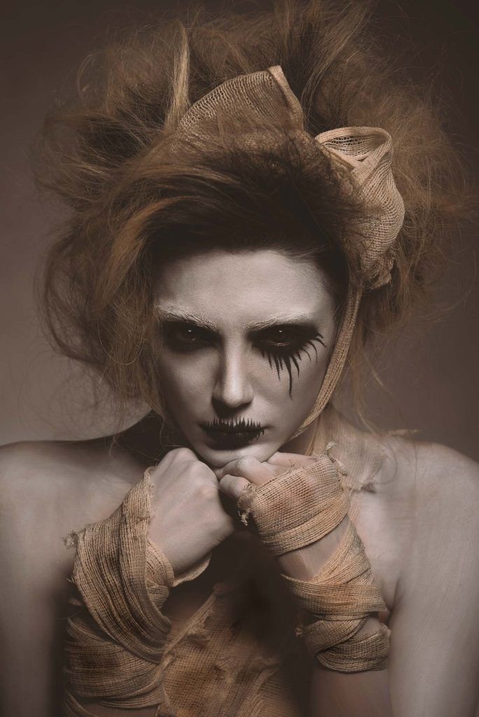Woman with dramatic dark theatrical makeup and burlap wrapped wrists in eerie artistic portrait.