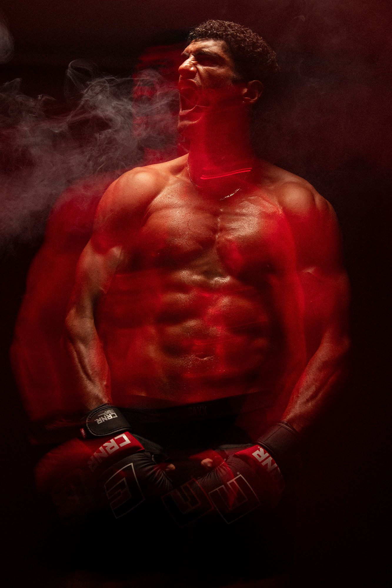 Muscular MMA fighter with boxing gloves poses shirtless in dramatic red smoke lighting.
