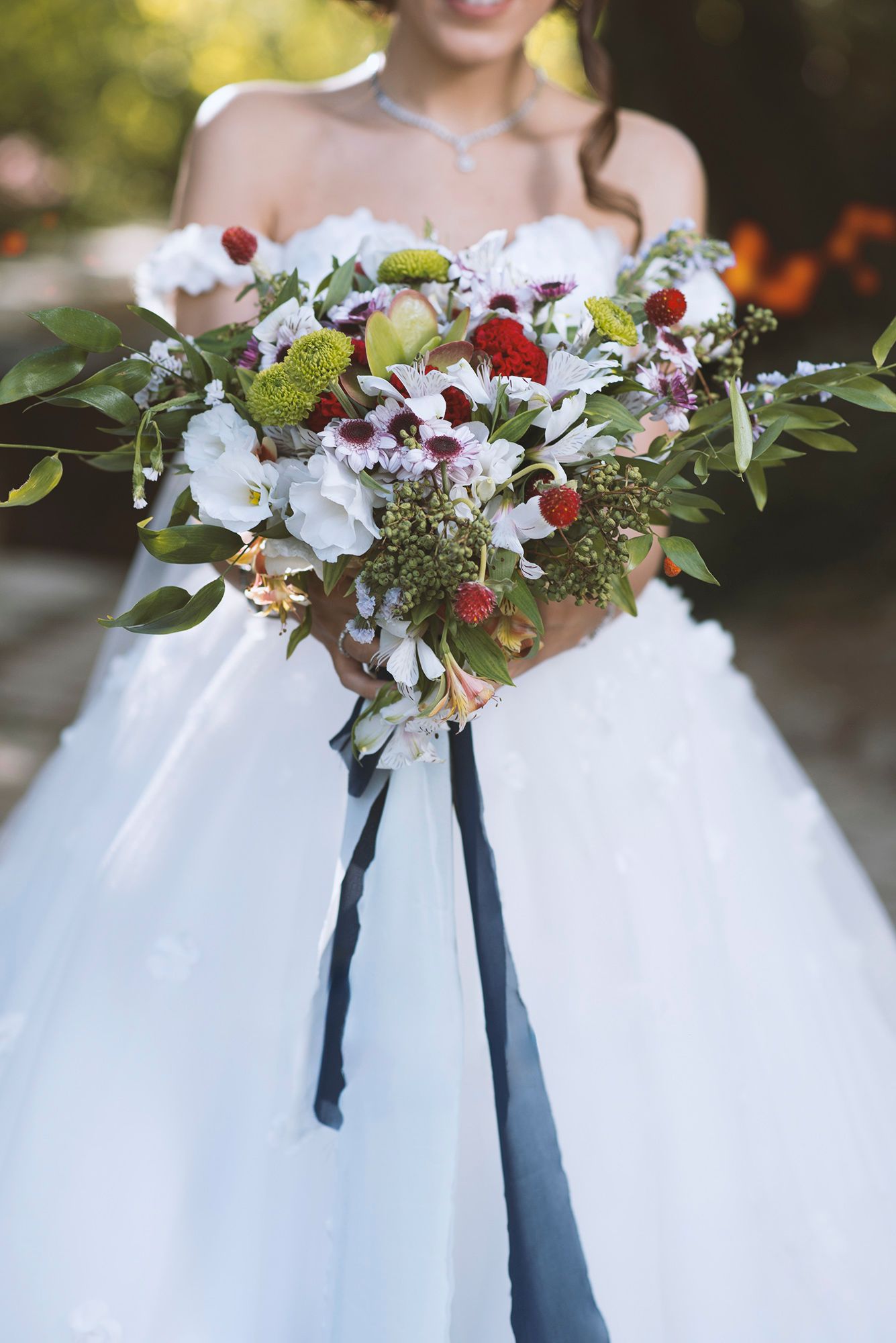 Bride in strapless ballgown holds lush wedding bouquet with white blooms, berries, and navy ribbon.