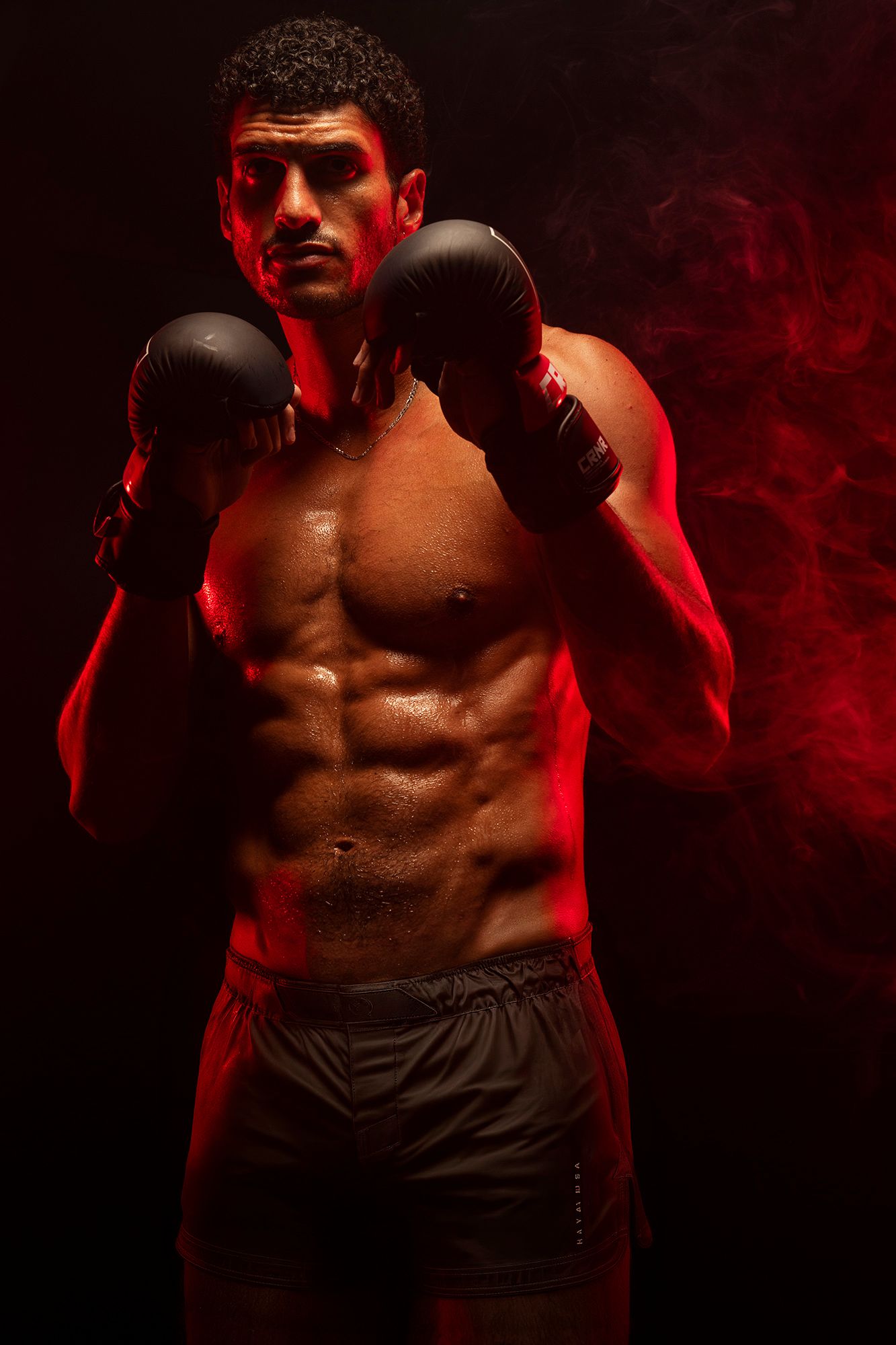 Shirtless male boxer in fighting stance with red smoke background.