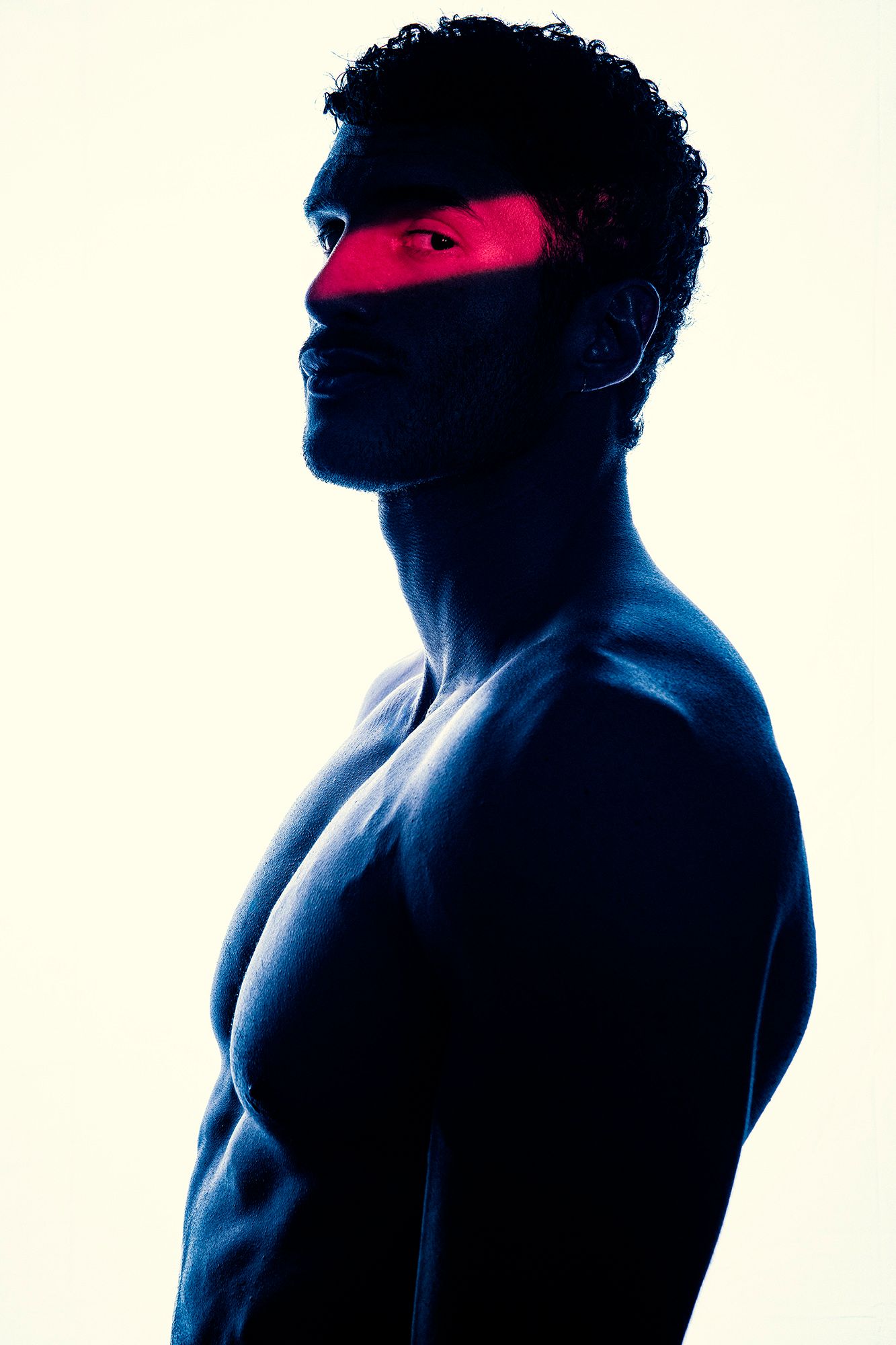 Artistic blue-toned silhouette of shirtless man with red light across eyes.