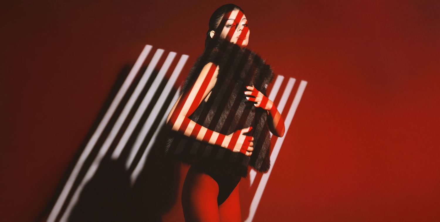 Silhouetted figure with striped light projection poses against vibrant red background.