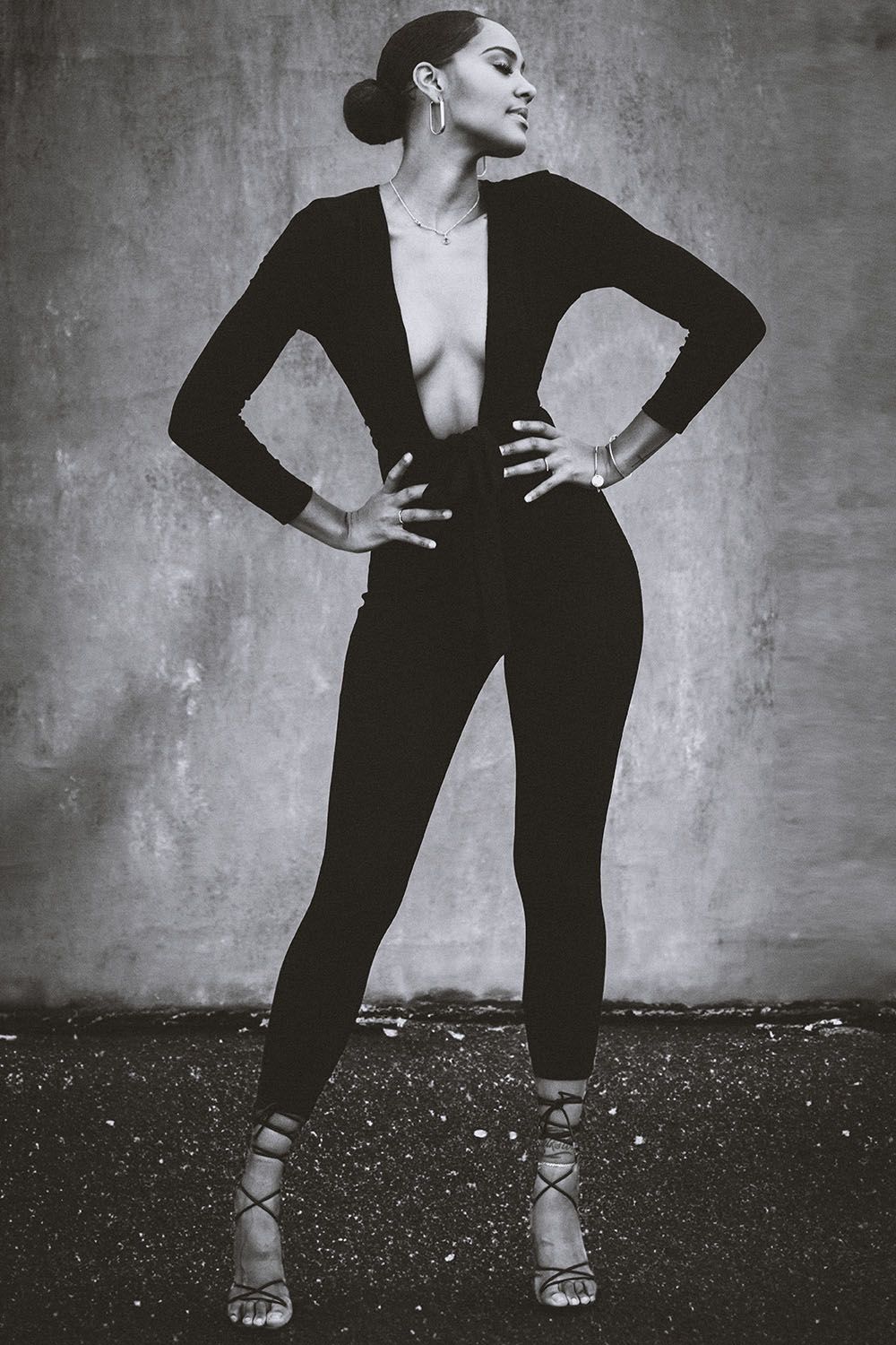 Confident woman in deep V black jumpsuit with hands on hips, black and white full body shot.