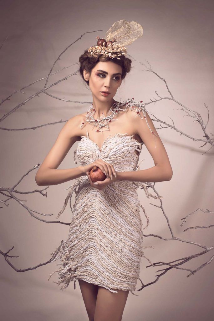 Fashion portrait of a model in a white feathered dress with an ornate headpiece holding an apple.