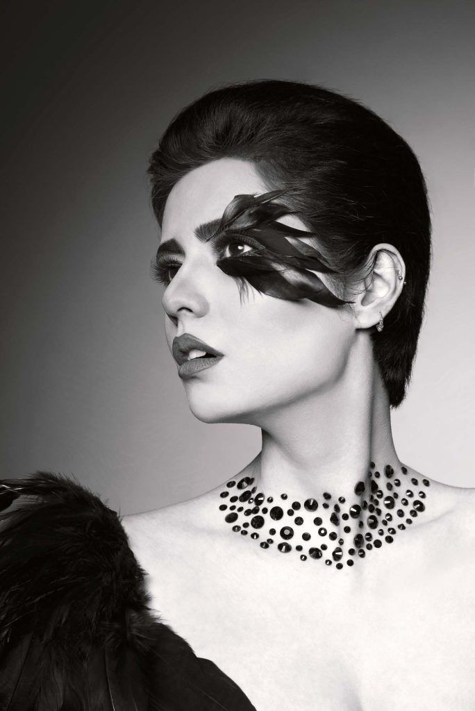Black and white portrait of woman with dramatic eye makeup and rhinestone necklace wearing fur.