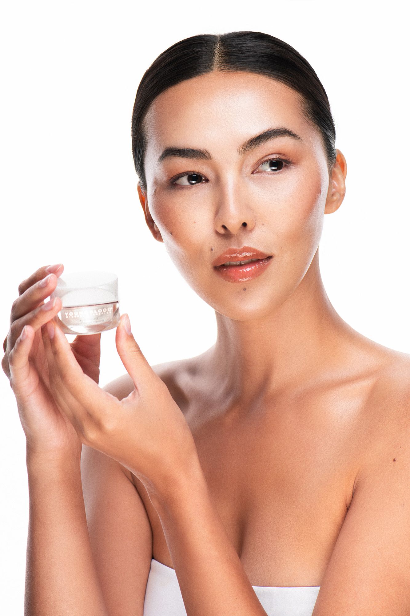 Young woman with clear skin holding a white cosmetic cream jar, showcasing skincare beauty product on white background.