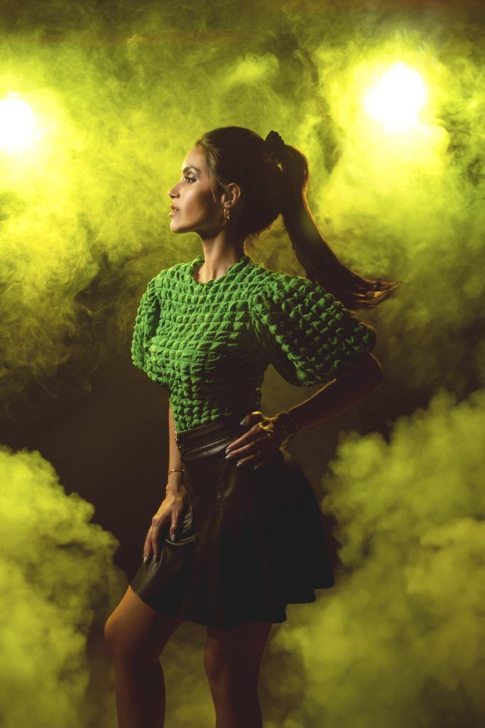 Fashion portrait of a woman in a green textured top posing dramatically in yellow smoke and light.