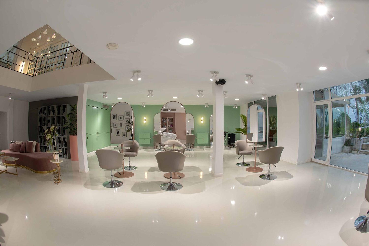 Modern hair salon interior with mint green walls, white floors, and stylish grey styling chairs under bright recessed lighting.
