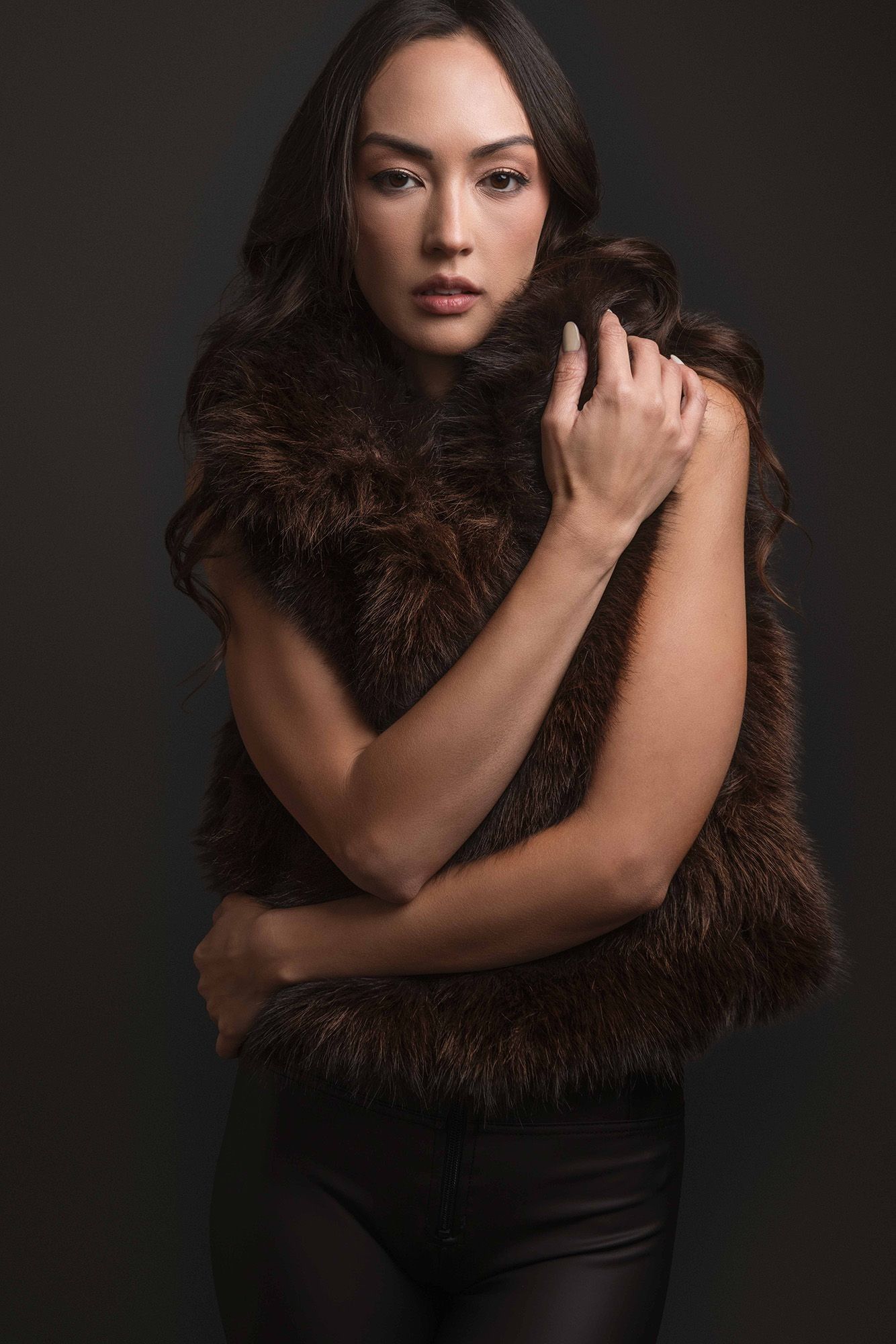 Woman in brown fur vest posing against dark background.