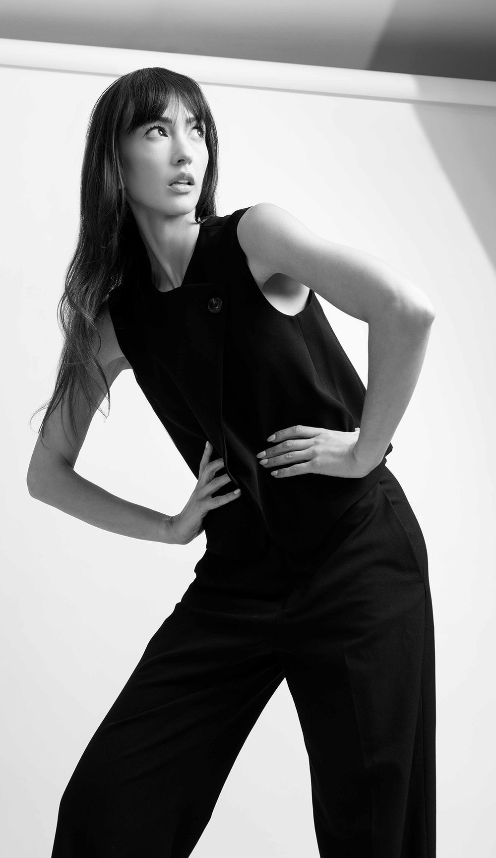 Black and white portrait of brunette model in sleeveless black outfit with dynamic pose.