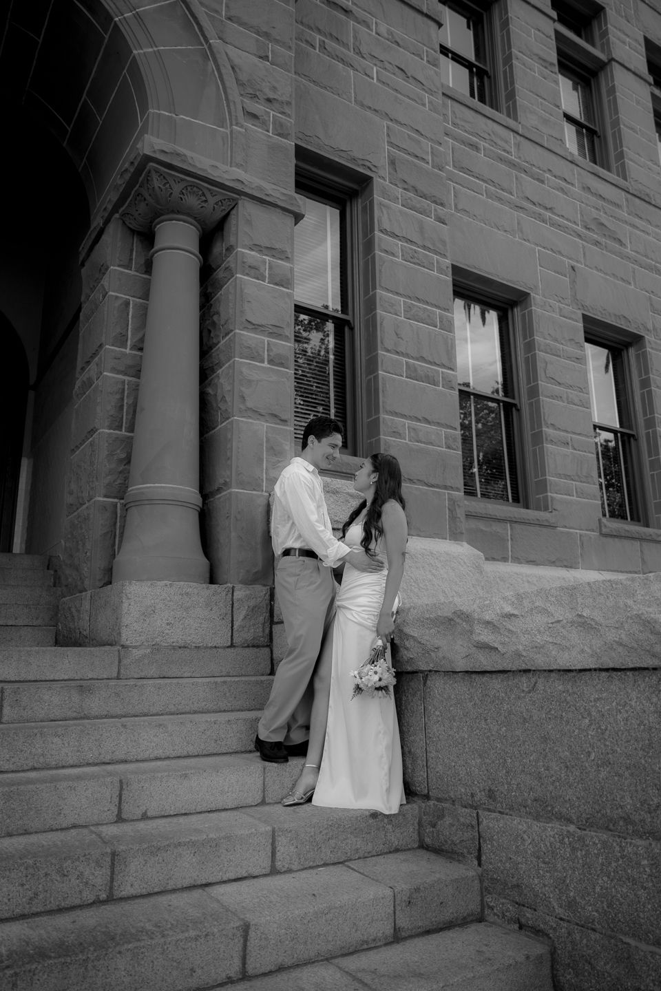 Black and white photo of a bride and groom sharing an intimate moment on stone steps of a historic building.