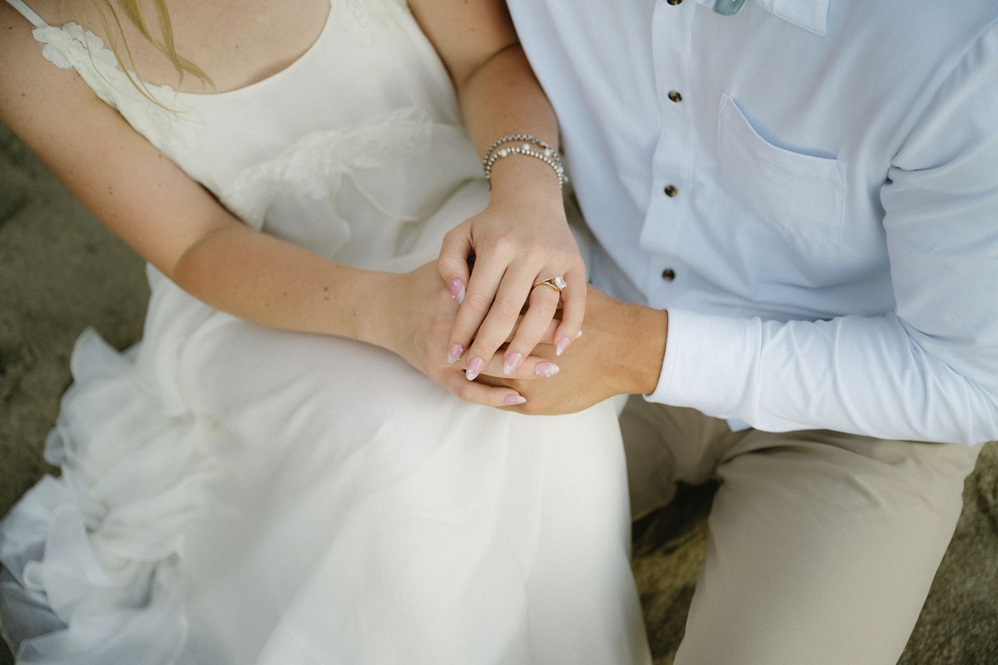 Bride and groom holding hands showing wedding ring, close-up of couple in white dress and blue shirt.