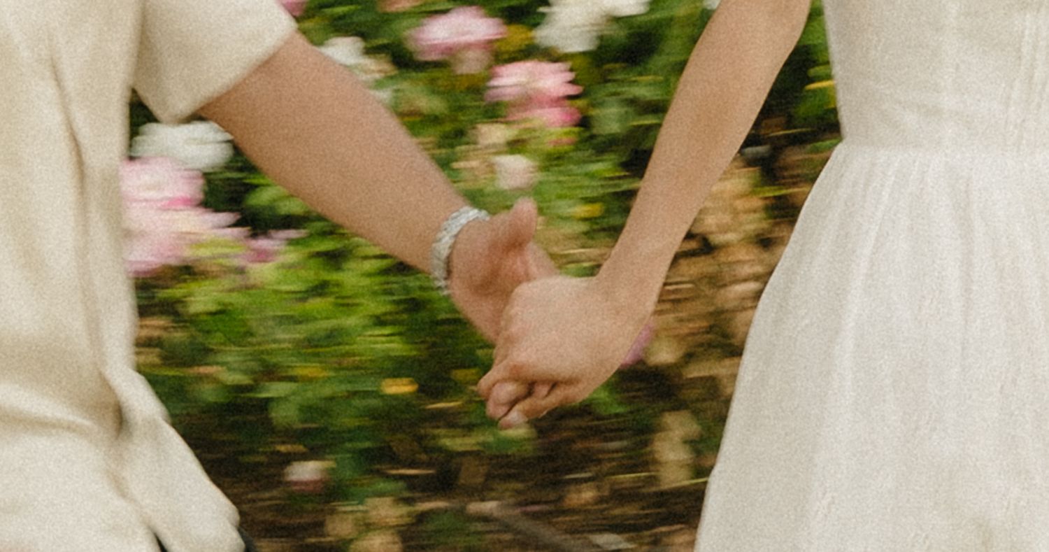 Couple holding hands in a romantic garden with blooming pink flowers in the background.