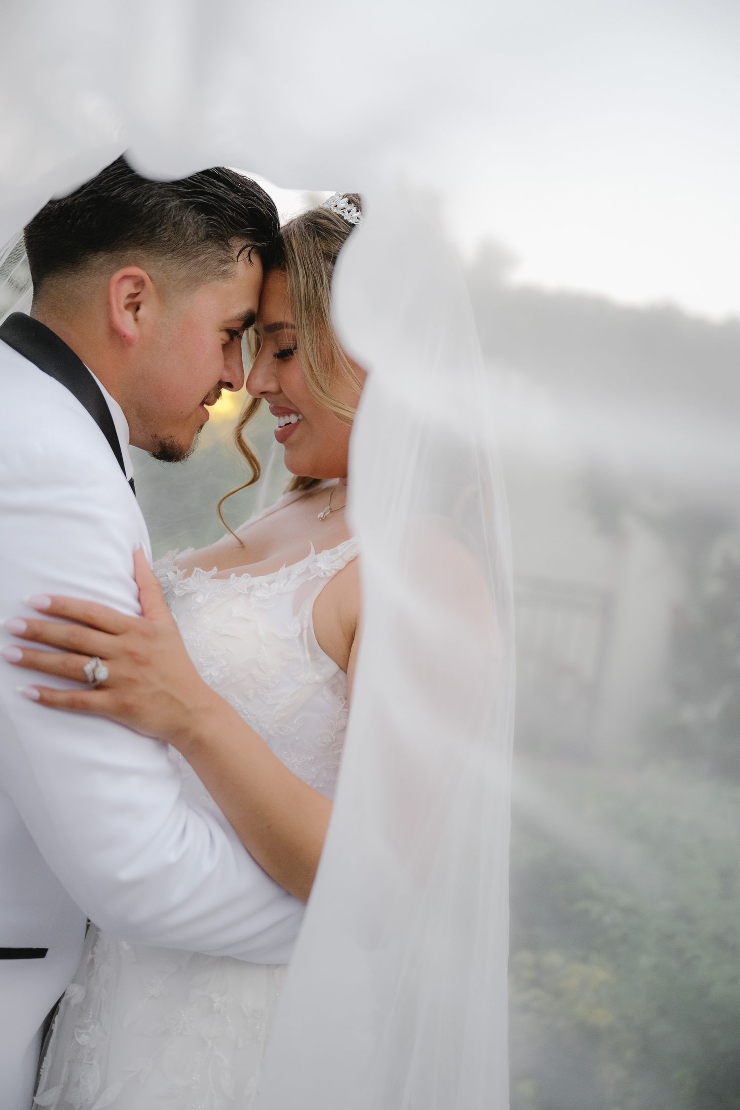 Bride and groom in wedding attire share a romantic kiss under veil