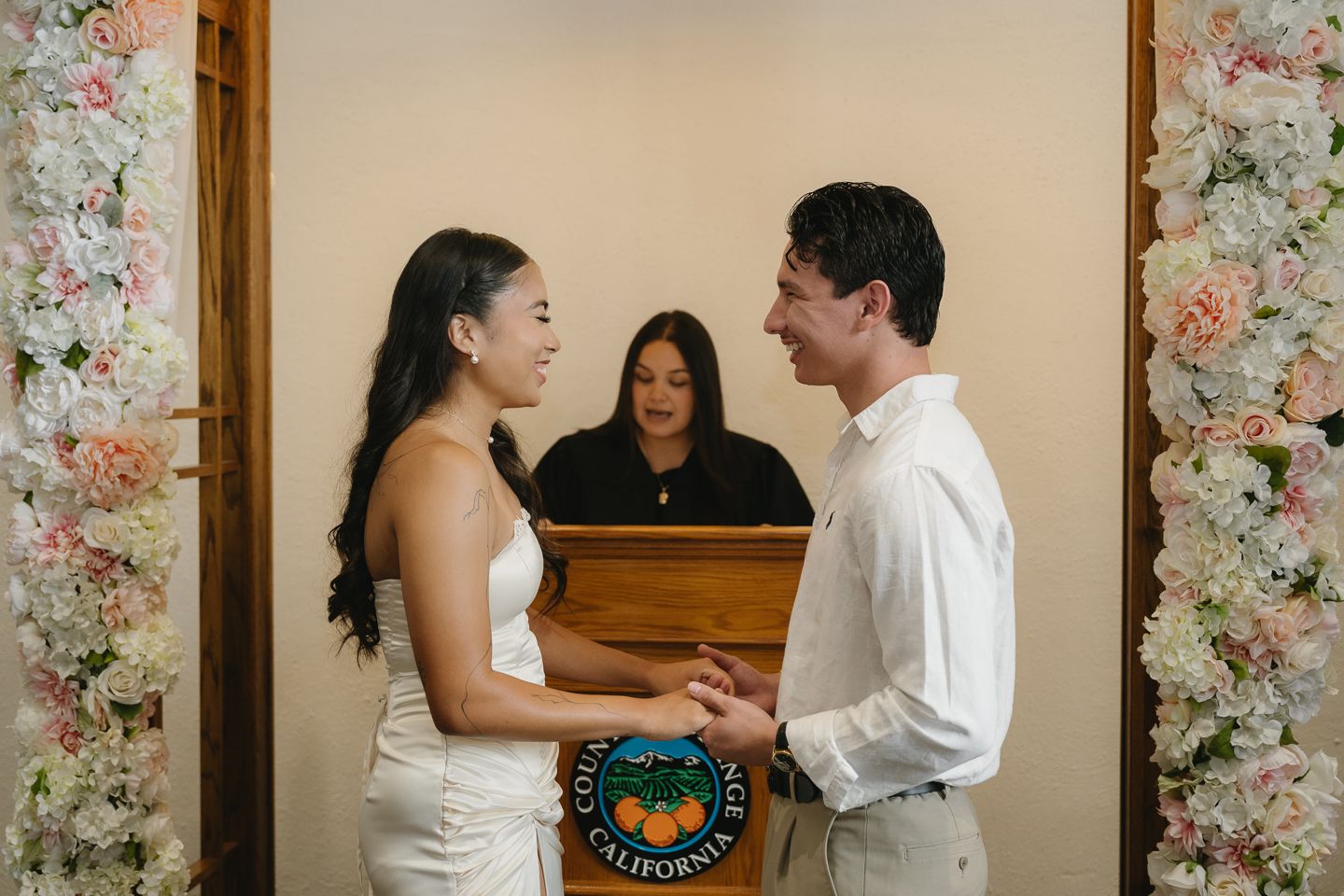 Couple exchanging vows at California wedding ceremony with officiant and floral arch backdrop.