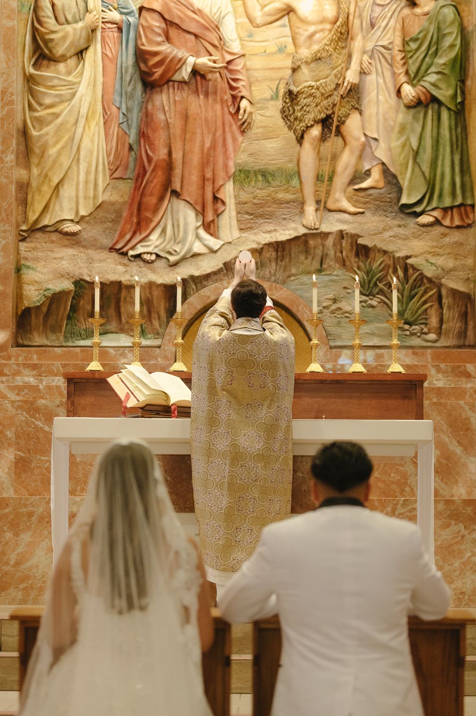 Bride and groom kneel before a priest at a Catholic wedding altar with eucharist.