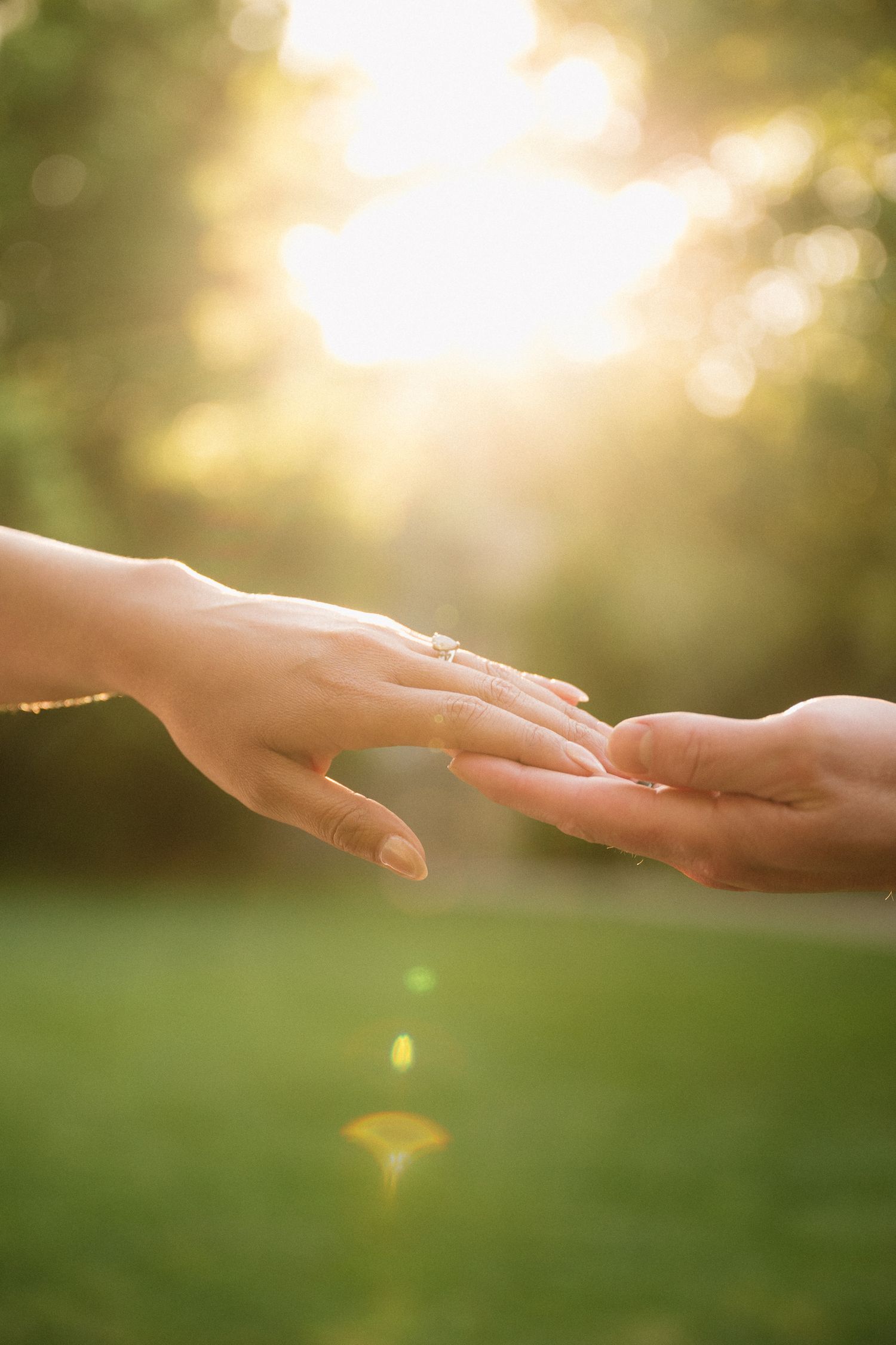 Two hands gently touching outdoors in golden sunlight, with an engagement ring visible on the woman's finger at Temecula wedding