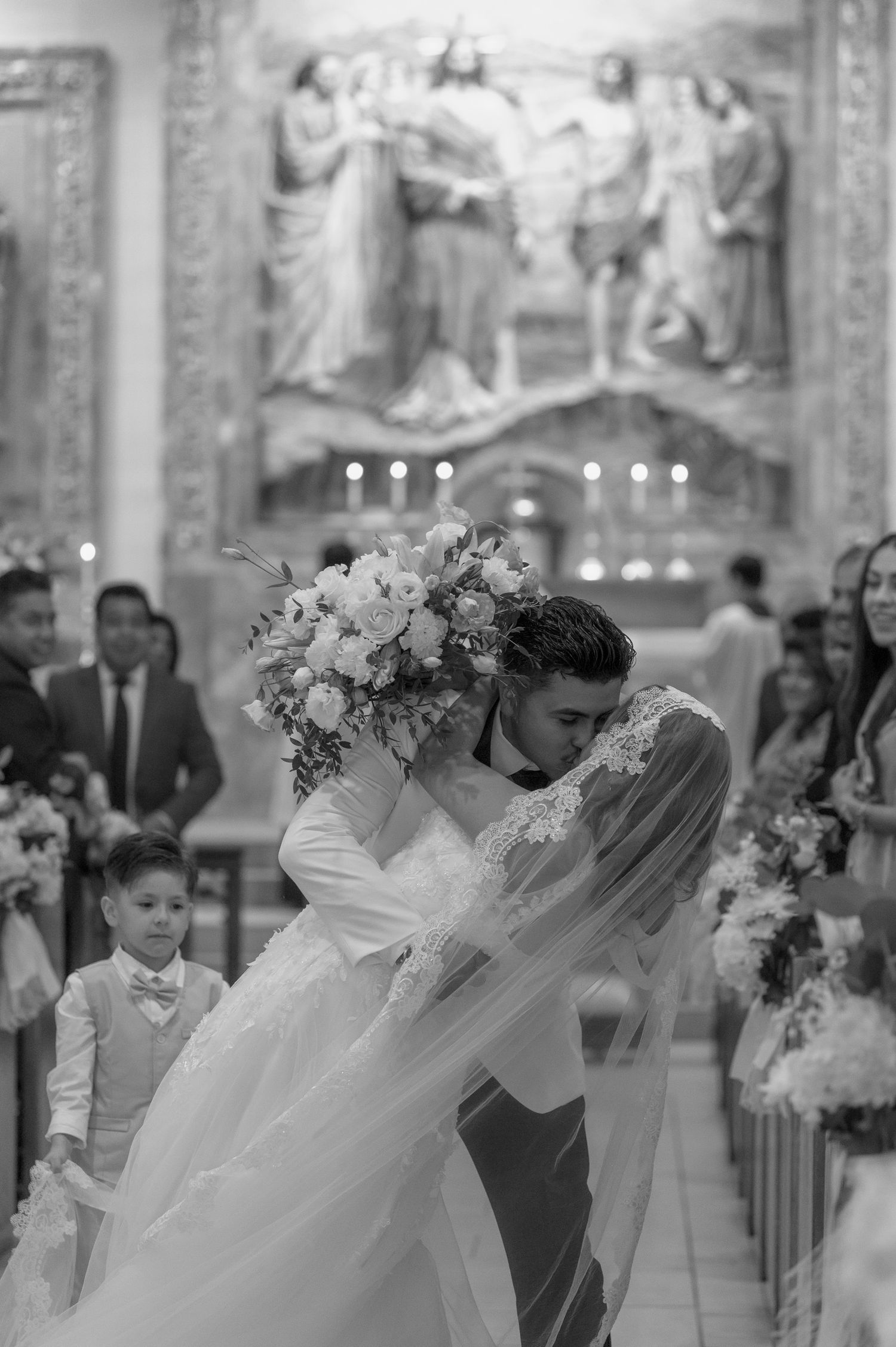 Black and white photo of a bride and groom sharing their first kiss at a church wedding ceremony.