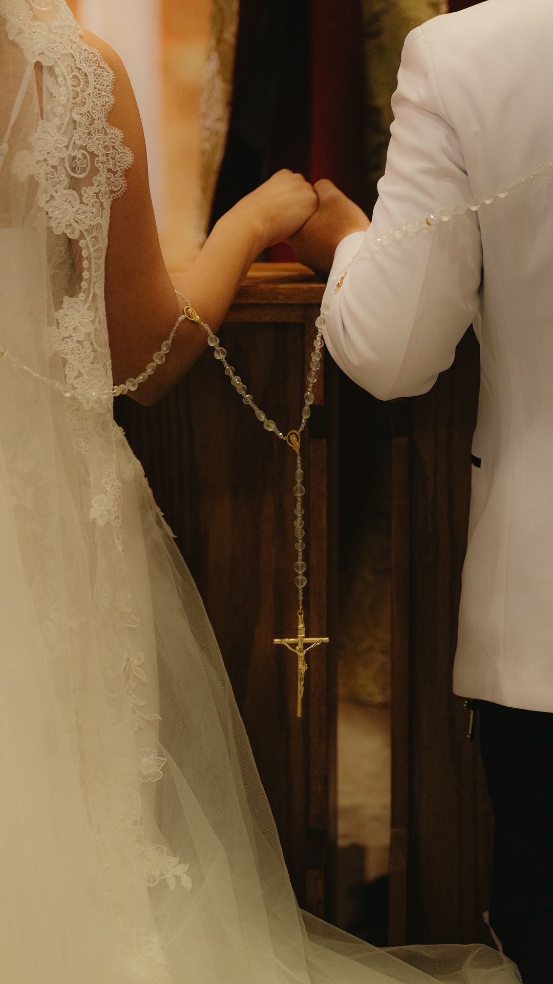 Bride and groom holding a gold rosary with crucifix at a church wedding ceremony altar.