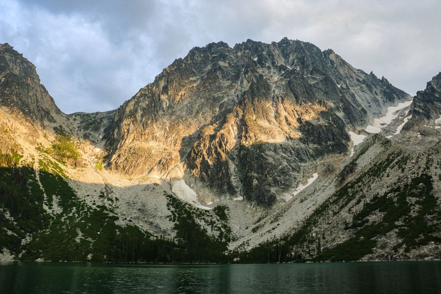 Dramatic rocky mountain peaks reflected in a glacial alpine lake under stormy clouds.